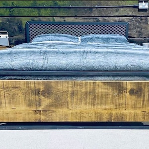 Puede incluir: Un marco de cama de metal con una cabecera de madera y una manta gris. El marco de la cama tiene una cabecera de malla de metal negro y una base de metal negro.