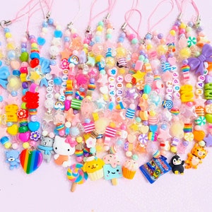 Può includere: Una collezione di ciondoli colorati per telefono con perline con vari ciondoli, tra cui stelle, fiocchi e personaggi dei cartoni animati. I ciondoli presentano una varietà di colori, tra cui rosa, blu, giallo e verde. Alcuni ciondoli hanno nomi scritti con perline bianche.