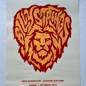 Puede incluir: Un póster rojo y amarillo con el texto "Billy Strings" en una fuente estilizada. El texto está dispuesto en un círculo alrededor de la cabeza de un león. El póster también incluye el texto "SWG3 Galvanizers - Glasgow, Escocia" y "Domingo 11 de diciembre de 2022".