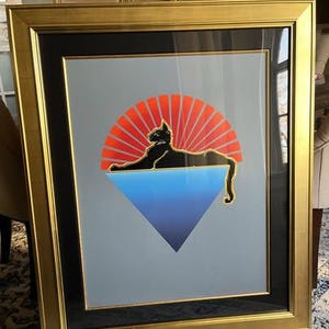 May include: A framed print of a black cat lying on a blue and purple triangle with a red and orange sunburst behind it.
