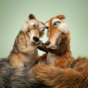 May include: Two plush squirrel-like figures with large eyes and long snouts. The left figure is light brown with a grey tail, while the right figure is reddish-brown with a large bushy tail and blue eyeshadow. Both have textured fur.