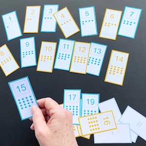 Op de afbeelding: Een set van 19 kaarten met de nummers 1 tot en met 19. Elke kaart heeft een in het blauw gedrukt nummer en een overeenkomend aantal blauwe of gele stippen.