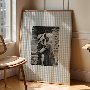 May include: A black and white photograph of a woman and a child in a gingham frame. The woman is holding the child in her arms and they are both looking at the camera. The photo is set against a backdrop of a checkered pattern.