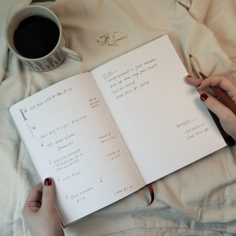 May include: An open notebook with handwritten notes, a cup of coffee, and a pen. The notebook's pages display a to-do list and reminders. The coffee cup has a gray and white pattern. The scene is set on a soft, white surface.