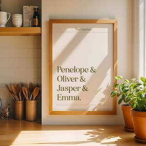Könnte beinhalten: Ein gerahmter Druck mit dem Text „The Lauries“ oben und den Namen Penelope, Oliver, Jasper und Emma in grüner Schrift. Der Rahmen ist aus hellem Holz, und der Druck wird auf einer Holztheke ausgestellt.