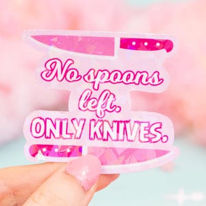 Puede incluir: Una pegatina holográfica rosa con el texto "No spoons left. ONLY KNIVES." La pegatina presenta dos ilustraciones de cuchillos rosas. El fondo es rosa y blanco.