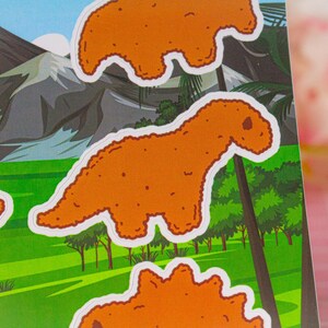 May include: A set of five orange dinosaur-shaped stickers. The dinosaurs are in various poses, including standing, walking, and running. The stickers are on a green background with a mountain range in the background.