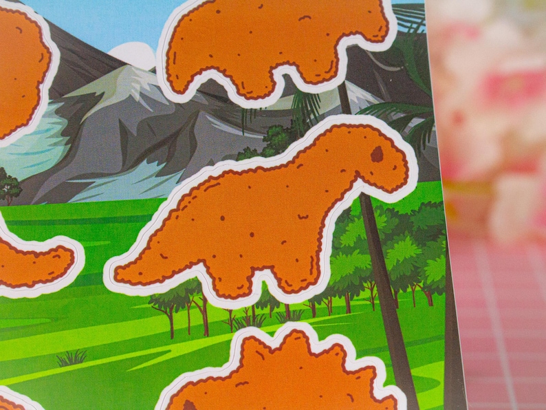 May include: A set of five orange dinosaur-shaped stickers. The dinosaurs are in various poses, including standing, walking, and running. The stickers are on a green background with a mountain range in the background.