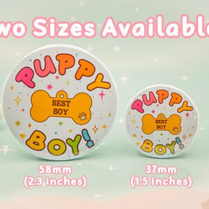 Op de afbeelding: Twee ronde buttons met de tekst "PUPPY BOY!" in roze, oranje en groen. De buttons zijn wit met een bot-afbeelding en steraccenten. De grotere button is 58 mm, de kleinere 37 mm.