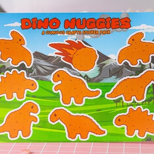 May include: A sticker pack featuring eight dinosaur-shaped chicken nuggets. The stickers are orange and have a cartoonish style. The text "Dino Nuggiges" and "A Cumulus Crafts Sticker Pack" is printed on the sticker sheet.