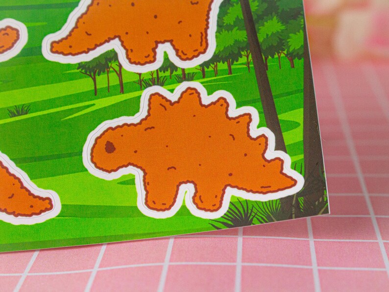 May include: A set of four orange dinosaur stickers with white outlines. The dinosaurs are in various poses, including standing, walking, and running. The stickers are on a green background with trees and bushes.