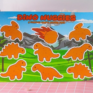 May include: A sheet of stickers featuring cartoon dinosaur-shaped chicken nuggets. The stickers are orange and yellow and have the text "Dino Nuggiges A Cumulus Crafts Sticker Pack".