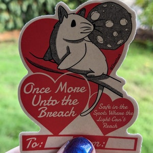 May include: A vintage-style Valentine's Day card featuring a cartoon mouse and a moon illustration. The card is heart-shaped with the text "Once More Unto the Breach" and "Safe in the Spots Where the Light Can't Reach". Includes space to write "To:" and "From:"