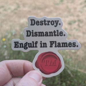 May include: A die-cut sticker featuring the black text "Destroy. Dismantle. Engulf in Flames." arranged in three lines above a circular red wax seal graphic that contains the embossed letters "TM" in the center of the wax seal design.