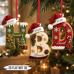 Könnte beinhalten: Drei hängende Weihnachtsschmuckstücke in Form der Buchstaben H, B und D. Jeder Buchstabe ist mit einer rot karierten Weihnachtsmannmütze, der Jahreszahl 2026 und festlichen Details wie Lebkuchenmännern, Tannenbäumen, Schneeflocken und Namen versehen.