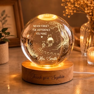 Könnte beinhalten: Ein kugelförmiges Glas-Nachtlicht auf einem runden Holzsockel. Das Glas zeigt eine Gravur von zwei Bären, einem Baum und dem Text: NEVER FORGET THE DIFFERENCE YOU MAKE, Mrs. Smith. Der Holzsockel ist graviert mit: Thank you Sophia.