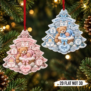 Könnte beinhalten: Zwei baumförmige Weihnachtsschmuckstücke mit einem schlafenden Baby im Korb und einem Teddybären. Das rosa Ornament zeigt Emma, 10. Oktober, 7lbs 6oz, 20,3 Zoll, Nashville, TN, 5:20 Uhr. Das blaue zeigt Noah mit identischen Details.