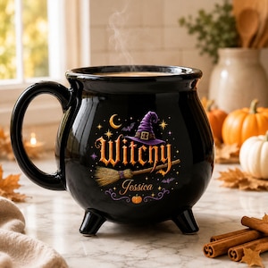 Può includere: Una tazza in ceramica nera a forma di calderone con tre piedini e un grande manico. La parte anteriore presenta una grafica con un cappello da strega viola, una scopa, una luna crescente, pipistrelli e la scritta "Witchy" e "Jessica".