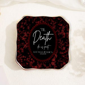 Könnte beinhalten: Ein quadratischer Untersetzer mit goldenem Rand und einem schwarz-roten Blumendesign. Das ovale Zentrum enthält den Text "'Til Death do us part" mit den Namen Lucas & Jessica und dem Datum 23.12.2026.