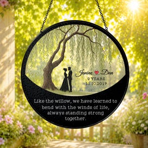 May include: A circular hanging ornament with a black frame and chain. The centre features a willow tree illustration with a couple standing beneath it. Text reads: Janine and Dan, 9 YEARS, 11.10.2017, and: Like the willow, we have learned to bend.