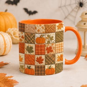 Könnte beinhalten: Ein Keramikbecher mit leuchtend orangefarbenem Innenraum und Henkel, der außen ein gestepptes Patchwork-Muster aufweist. Das Design besteht aus Quadraten mit Herbstblättern, Karomustern und orangefarbenen Kürbissen in Braun- und Goldtönen.