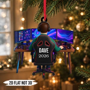 Könnte beinhalten: Ein flacher, zweidimensionaler Weihnachtsbaumschmuck, der eine Person mit Kopfhörern zeigt, die in einem schwarzen Gaming-Stuhl mit roten Akzenten sitzt. Auf der Rückenlehne steht der Text DAVE und 2026. Die Person sitzt vor drei Monitoren.