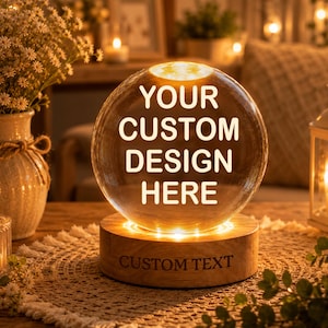 Puede incluir: Una lámpara de esfera de cristal transparente sobre una base circular de madera. La esfera presenta el texto blanco YOUR CUSTOM DESIGN HERE. La base de madera está iluminada desde abajo y tiene el texto grabado CUSTOM TEXT en el frente.