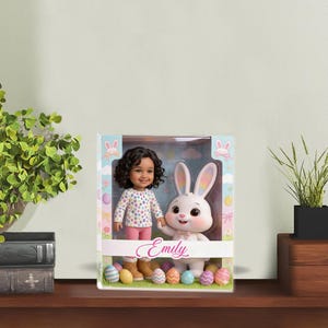 Könnte beinhalten: Ein Puppenset in einer Box mit einer Puppe mit lockigem Haar und einem weißen Hasen. Die Puppe trägt ein gepunktetes Hemd und eine rosa Hose. Der Hase ist weiß mit rosa Akzenten. Die Box trägt den Namen "Emily" und Ostereier-Dekorationen.