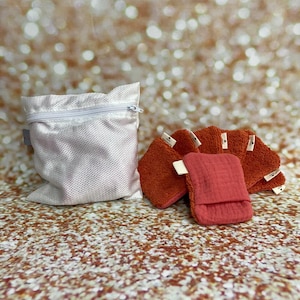 Puede incluir: Un juego de seis paños reutilizables de color naranja y rojo en una bolsa de lavandería de malla blanca. Los paños están hechos de un material suave y absorbente, ideales para limpiar y secar.