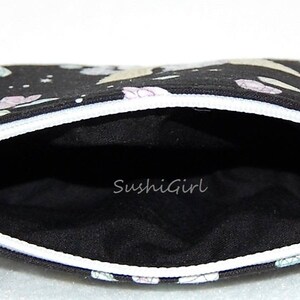 Puede incluir: Bolsa negra con cremallera blanca y forro negro. La bolsa tiene un estampado colorido de unicornios y estrellas. El texto "SushiGirl" est&aacute; impreso en el forro.