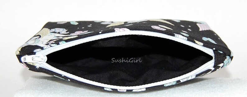 Puede incluir: Bolsa negra con cremallera blanca y forro negro. La bolsa tiene un estampado colorido de unicornios y estrellas. El texto "SushiGirl" est&aacute; impreso en el forro.