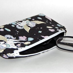 Puede incluir: Bolsa negra con cremallera blanca y estampado de unicornio blanco y negro. La bolsa est&aacute; llena de un par de gafas con montura negra.