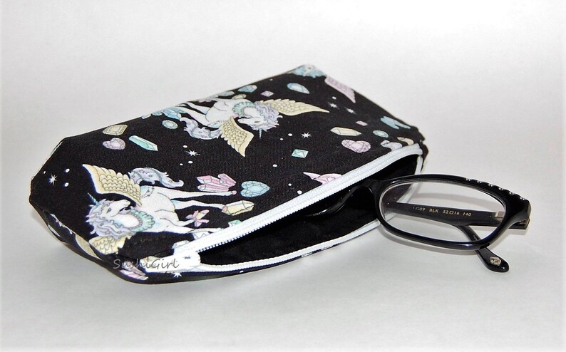 Puede incluir: Bolsa negra con cremallera blanca y estampado de unicornio blanco y negro. La bolsa est&aacute; llena de un par de gafas con montura negra.