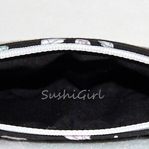 Puede incluir: Bolsa negra con cremallera blanca y dise&ntilde;o estampado en blanco y negro. El interior de la bolsa es negro y tiene el texto "SushiGirl" impreso en blanco.