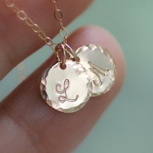May include: Gold necklace with two round pendants, one with the letter "L" and the other with the letter "M".
