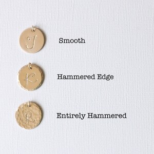 May include: Three gold-toned metal discs with different finishes. The top disc is smooth, the middle disc has a hammered edge, and the bottom disc is entirely hammered. Each disc has a letter engraved on it: "J", "K", and "R".