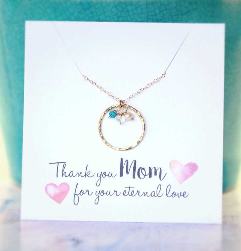 May include: A gold necklace with a circle pendant and turquoise and white beads. The necklace is displayed on a white card with the text "Thank you Mom for your eternal love" and two pink hearts.