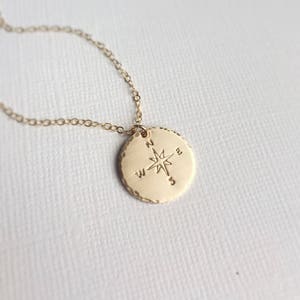 Puede incluir: Collar de oro con un colgante redondo de br&uacute;jula con una estrella y las letras N, S, E y W.