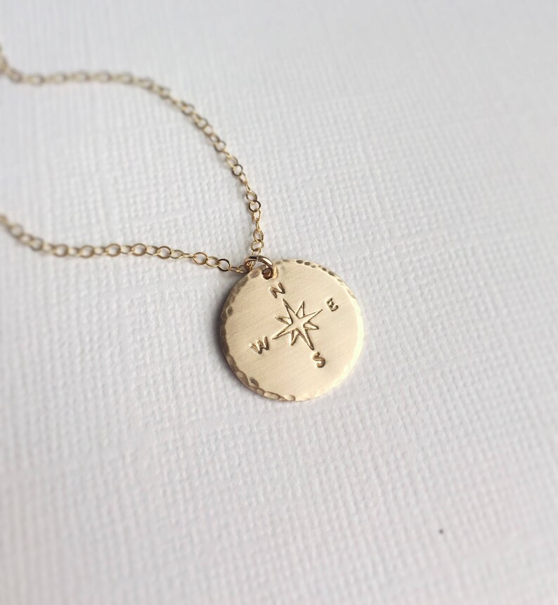 Puede incluir: Collar de oro con un colgante redondo de br&uacute;jula con una estrella y las letras N, S, E y W.