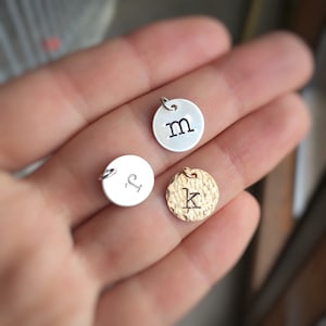 May include: Three silver and gold charms with initial letters 'M', 'P', and 'K' engraved on them. The charms are round and have a hammered texture.