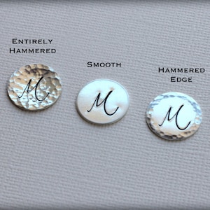 May include: Three silver metal pendants with the letter "M" in a script font. One pendant is entirely hammered, one is smooth, and the third has a hammered edge. The text "ENTIRELY HAMMERED", "SMOOTH", and "HAMMERED EDGE" are above each pendant.