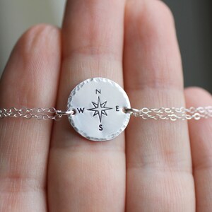 May include: Silver necklace with a compass charm featuring a star and the letters N, S, E, and W.