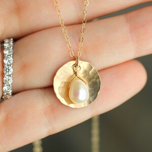 May include: A gold necklace with a hammered disc pendant and a single pearl hanging from it.