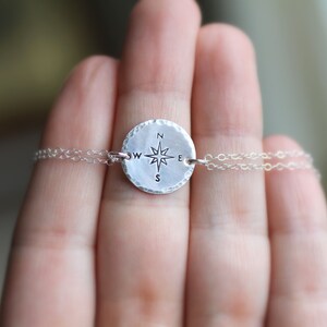 May include: A silver necklace with a round compass charm featuring a star and the letters N, S, E, and W.