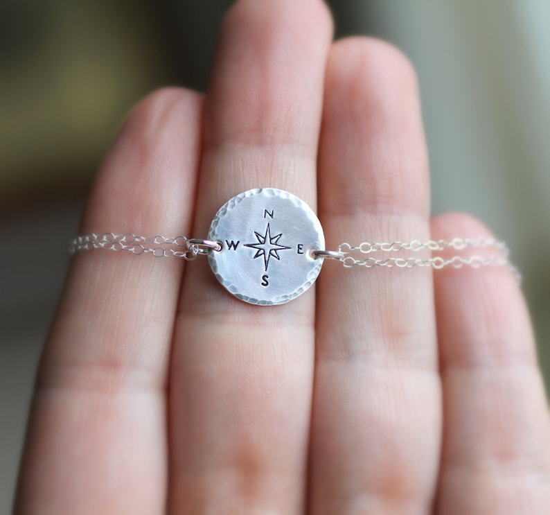 May include: A silver necklace with a round compass charm featuring a star and the letters N, S, E, and W.
