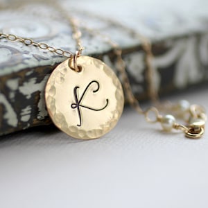 May include: Gold necklace with a hammered round pendant featuring a cursive letter K.