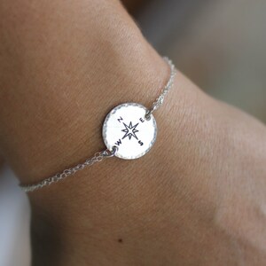May include: A silver chain bracelet with a round compass charm. The compass charm has a star in the centre and the letters N, S, E, and W around the edge.