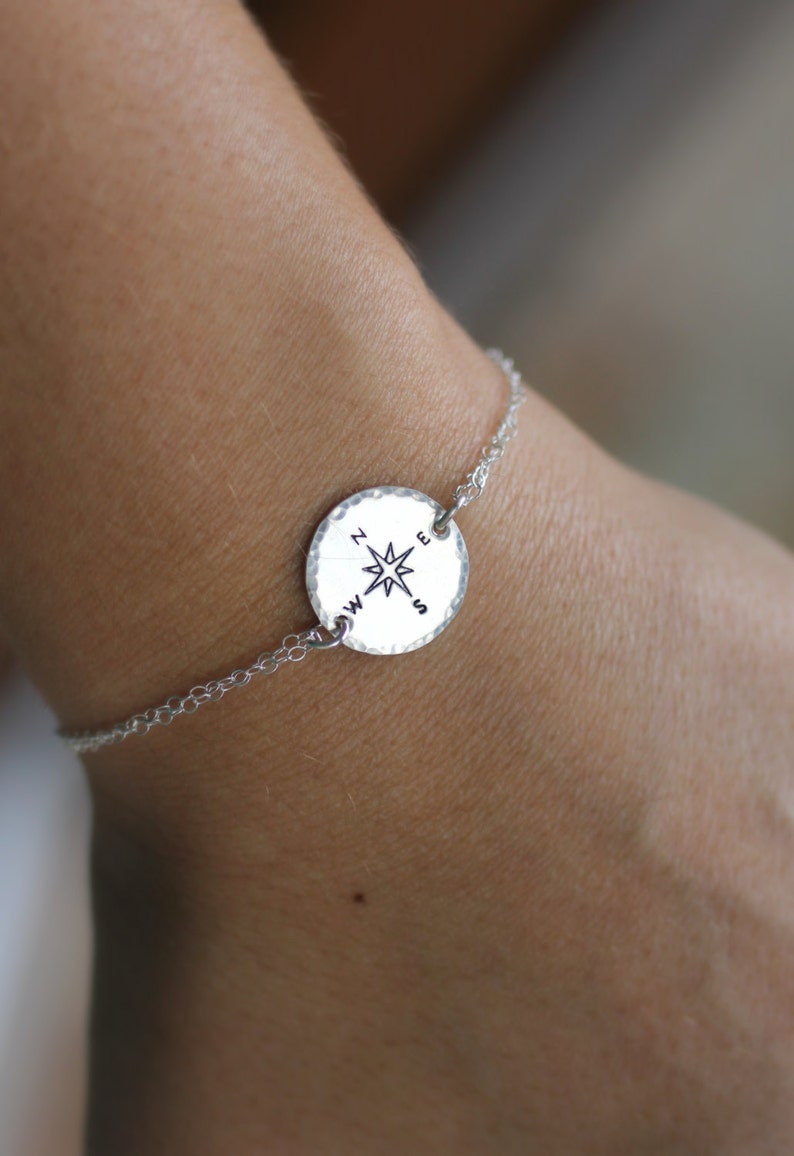 May include: A silver chain bracelet with a round compass charm. The compass charm has a star in the centre and the letters N, S, E, and W around the edge.