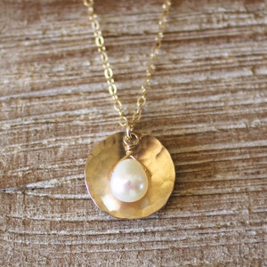 May include: A gold chain necklace with a hammered gold pendant featuring a single white pearl.