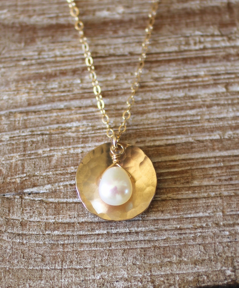 May include: A gold chain necklace with a hammered gold pendant featuring a single white pearl.
